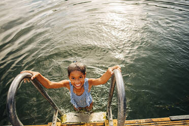 High angle view of smiling girl holding railing while standing near steps in lake - MASF32617