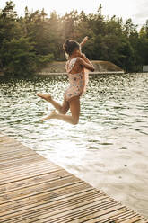 Carefree girl jumping in lake from jetty during vacation - MASF32646