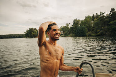 Glücklicher Mann ohne Hemd und mit dem Kopf in der Hand beim Schwimmen am See im Urlaub - MASF32657
