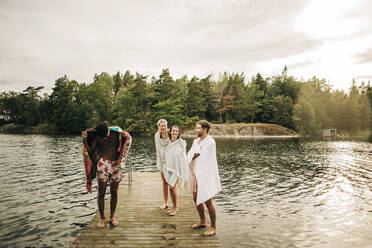 Glückliche Freunde, die ein Handtuch tragen, während sie im Urlaub auf dem Steg am See stehen - MASF32661