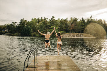 Rückansicht von Freundinnen im Bikini beim Springen im See im Urlaub - MASF32662