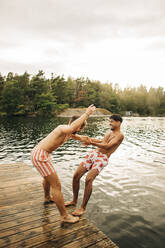 Side view of man at jetty pushing male friend in lake during vacation - MASF32670