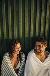 Lächelnder Mann und Frau, die ein Handtuch tragen, während sie bei Sonnenuntergang miteinander sprechen - MASF32689