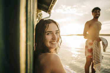 Porträt einer glücklichen Frau, die im Urlaub bei Sonnenuntergang über die Schulter schaut - MASF32697