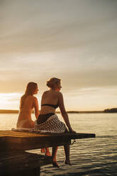 Frauen sitzen bei Sonnenuntergang auf einem Steg am See - MASF32708