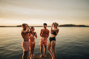 Glückliche junge Männer und Frauen, die sich auf einem Steg am See unterhalten, während sie im Urlaub sind - MASF32713