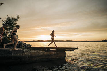 Friends running on jetty towards lake during vacation on sunset - MASF32717