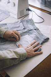 Hände eines Modedesigners beim Einstellen der Gesäßtasche einer Jeans in einem Workshop - MASF32723