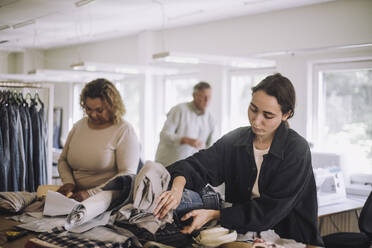 Young female fashion designer examining clothes while working at workshop - MASF32724