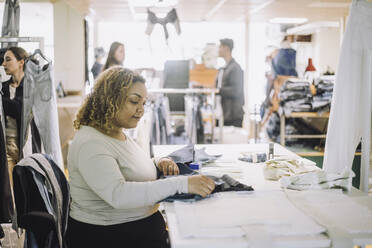 Seitenansicht einer jungen Modedesignerin, die bei der Arbeit im Atelier einen Stoff untersucht - MASF32744