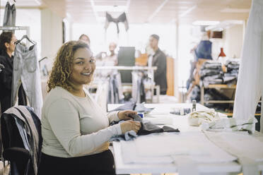 Porträt einer lächelnden Modedesignerin, die an einer Werkbank in einer Werkstatt sitzt - MASF32745