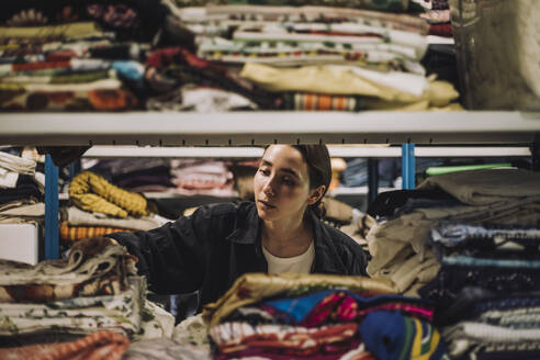 Weibliche Modedesignerin bei der Suche nach Kleidung auf einem Regal in einer Werkstatt - MASF32754