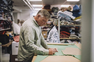 Side view of mature fashion designer marking on fabric while working at workshop - MASF32772