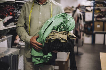 Mittelteil eines männlichen Modedesigners, der in einer Werkstatt Kleidung hält - MASF32773