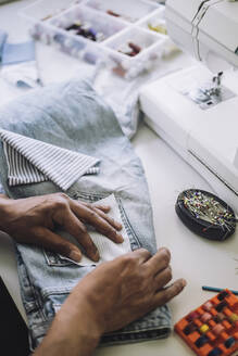 Blick von oben auf einen Modedesigner, der in einem Workshop Stoff auf die Gesäßtasche einer Jeans näht - MASF32774