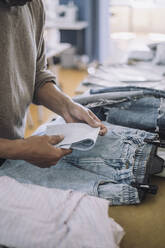 Männlicher Modedesigner faltet Stoff mit Jeans auf einer Werkbank in einer Werkstatt - MASF32791