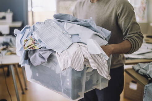 Mittelteil eines männlichen Modedesigners, der recycelte Kleidung in einem Container hält - MASF32792