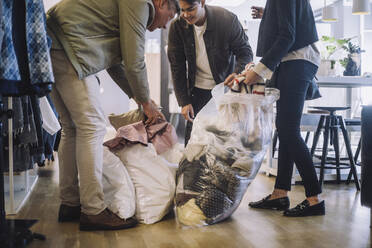 Fashion designers removing recycled clothes from plastic bags at workshop - MASF32806