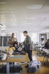 Männliche Design-Profis sortieren in einem Workshop recycelte Kleidung - MASF32816