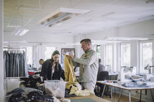 Männliche und weibliche Design-Profis sortieren in der Werkstatt recycelte Kleidung aus - MASF32818