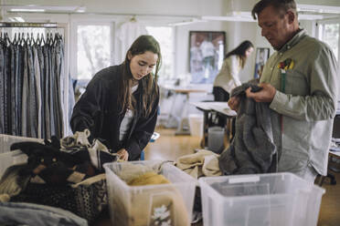 Female fashion designer with male colleague sorting recycled clothes while working at workshop - MASF32819