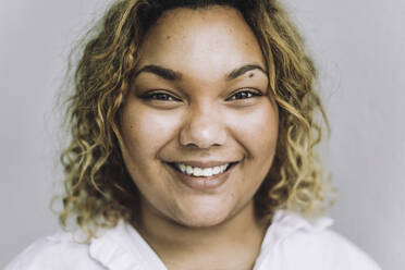 Portrait of happy fashion designer with curly hair against gray background - MASF32830