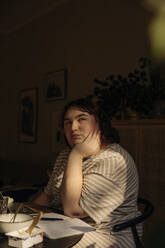 Nachdenkliche junge Frau sitzt mit dem Kopf in den Händen am Tisch - MASF32836