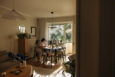 Full length of young woman sitting at table in living room - MASF32844