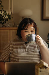 Junge Frau trinkt Kaffee und benutzt einen Laptop zu Hause - MASF32910
