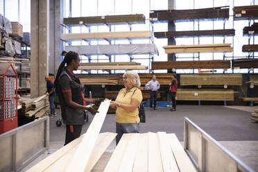 Saleswoman smiling while explaining female customer holding plank in trailer at hardware store - MASF32944