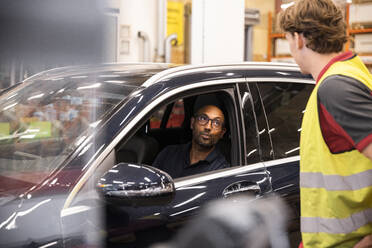 Männlicher Kunde im Auto im Gespräch mit dem Verkaufspersonal am Kassenschalter - MASF32995