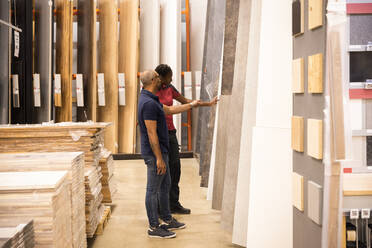 Side view of male customer with saleswoman choosing laminated boards at hardware store - MASF33006