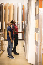 Customer and sales staff looking up while selecting laminated boards at hardware store - MASF33007