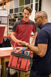 Male cashier talking to mature customer holding basket while standing at checkout in hardware store - MASF33015