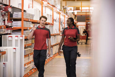 Male and female sales staff talking while walking in hardware store - MASF33022