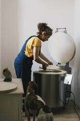 Seitenansicht einer Handwerkerin, die bei ihrer Arbeit zu Hause eine Keramikplatte in einen elektrischen Brennofen legt - MASF33062