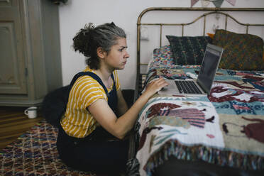 Woman sitting on floor using laptop in bedroom at home - MASF33066