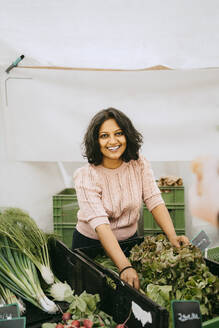 Porträt einer lächelnden Besitzerin in der Nähe einer Gemüsekiste an einem Marktstand - MASF33120