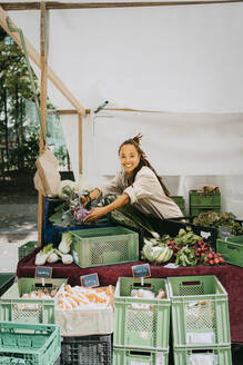 Lächelnde Besitzerin beim Aufbau eines Gemüsestandes auf dem Markt - MASF33122