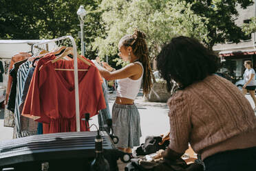 Seitenansicht einer Kundin, die beim Einkaufen auf einem Flohmarkt ein Kleid in ein Regal hängt - MASF33125