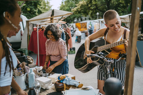 Smiling female customer playing guitar while shopping at flea market - MASF33130