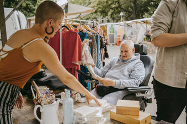 Weibliche Kundin mit Behinderung im Gespräch mit dem Besitzer beim Einkaufen auf dem Flohmarkt - MASF33136