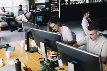 Female and male programmers coding on computers while working in startup company - MASF33185