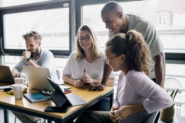 Happy female and male computer programmers planning strategy over laptop in startup company - MASF33197