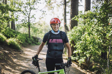 Porträt eines Mannes in Schutzkleidung, der mit einem Fahrrad auf einem Fußweg steht - MASF33202