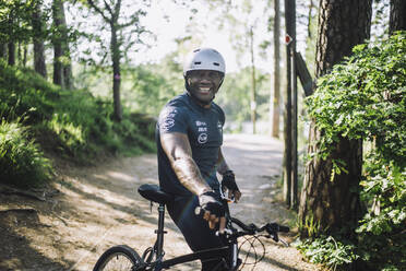 Porträt eines lächelnden Mannes, der sich auf dem Fußweg an ein Fahrrad lehnt - MASF33206