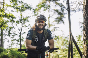 Lächelnder männlicher Radfahrer mit Helm, der sich auf sein Fahrrad stützt - MASF33212