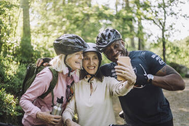Lächelnde ältere Frau nimmt Selfie durch Smartphone mit männlichen und weiblichen Freund - MASF33222