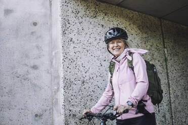 Porträt einer älteren Frau mit Fahrrad an der Wand stehend - MASF33223