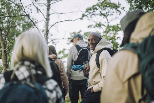 Porträt eines lächelnden Mannes mit Kapuzenhemd beim Wandern mit Freunden im Wald - MASF33275